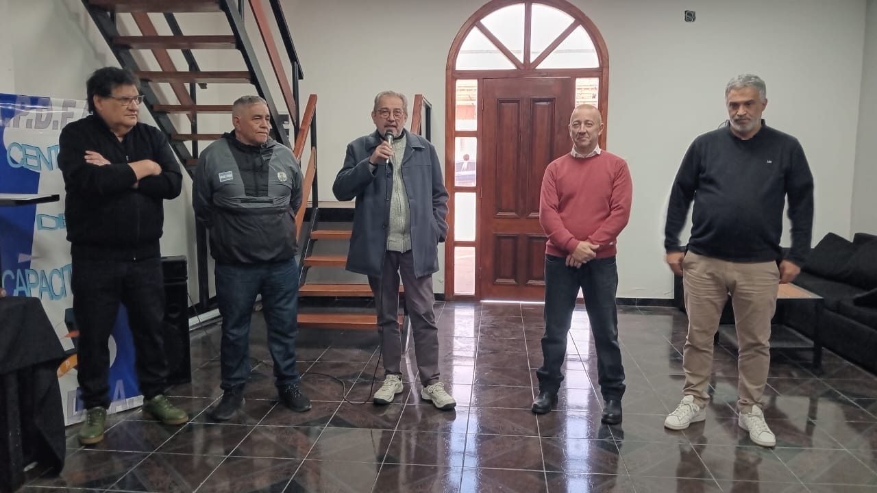 Cinco dirigentes de APDFA de pie en el salón de la jornada; uno de ellos habla por micrófono.