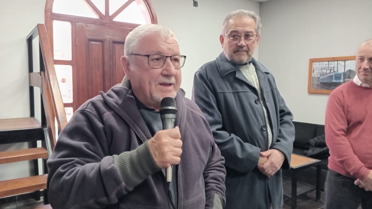 Un jubilado ferroviario habla por micrófono mientras otros dirigentes lo acompañan.