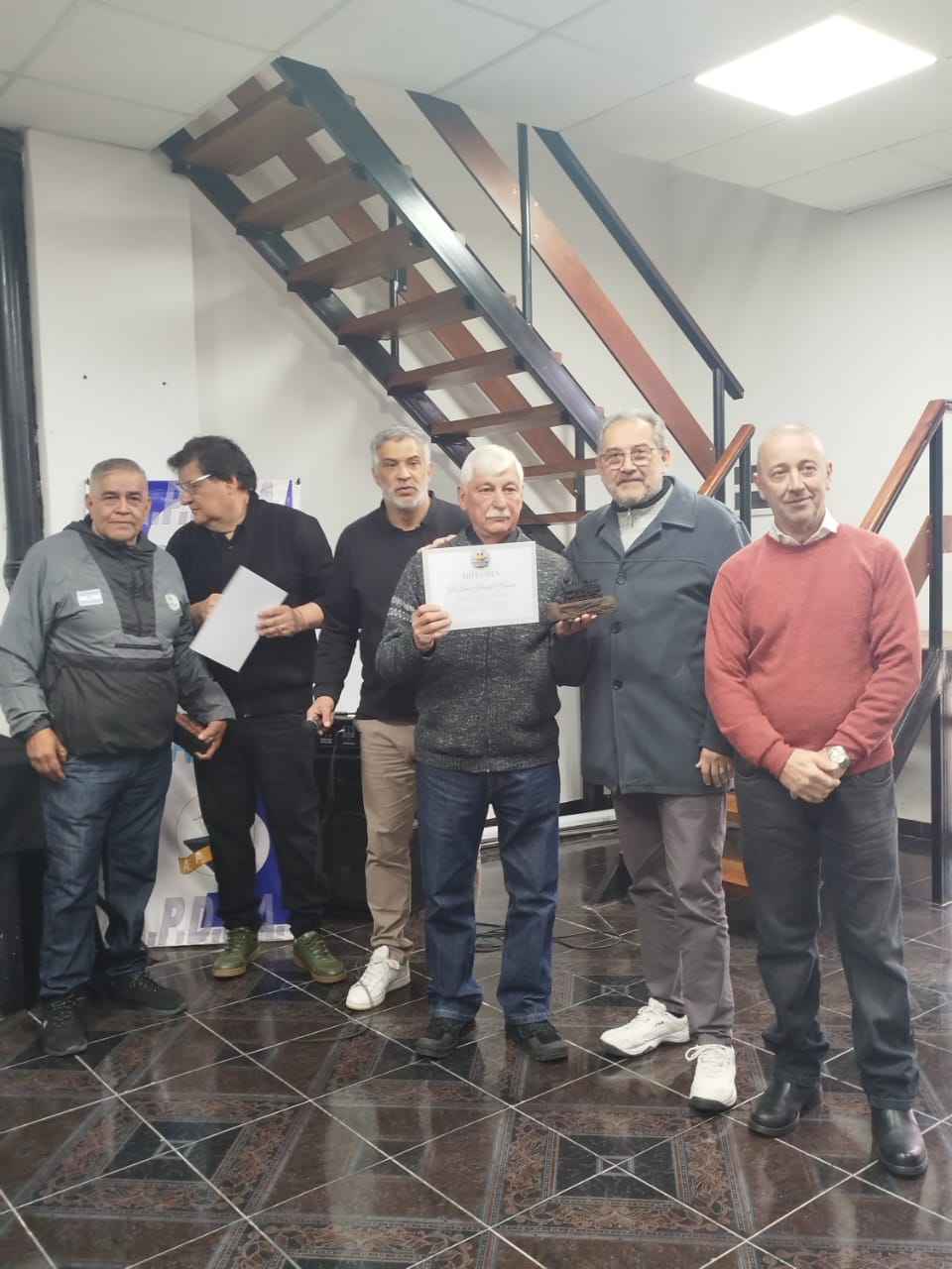 Un compañero jubilado sostiene su diploma y un recordatorio, acompañado por dirigentes de APDFA.